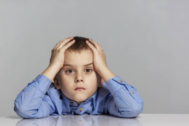 Üzgün liseli çocuk masaya oturur ve başını tutar. Öğrenme zorluğu. Gri arka plan. Metin için boşluk.