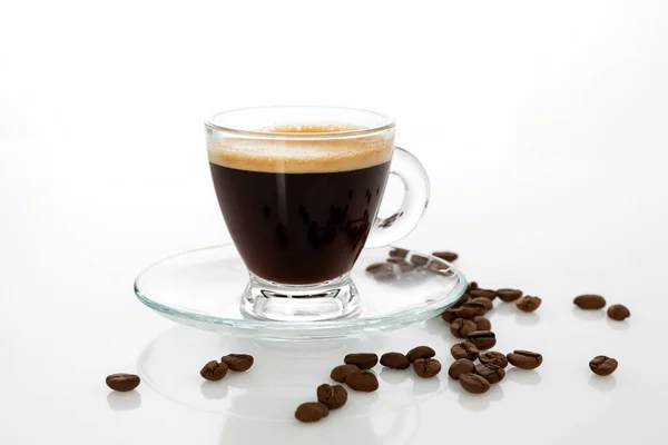 Şeffaf bir espresso bardağı ve masaya serpiştirilmiş fasulye. Beyaz arkaplan.