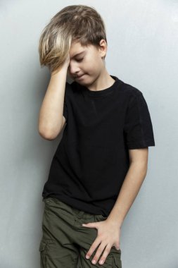 9 yaşında siyah tişörtlü üzgün bir çocuk başını eğip yere baktı. Yalnızlık, depresyon, salgın sırasında uzak eğitim. Gri arka plan. Dikey.