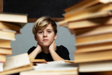 Üzgün çocuk kitaplarla dolu bir masada oturuyor. Depresyon, yalnızlık, öğrenme güçlüğü.