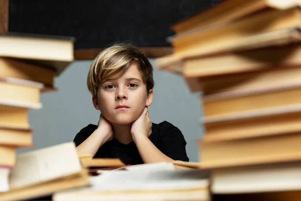 Üzgün çocuk kitaplarla dolu bir masada oturuyor. Depresyon, yalnızlık, öğrenme güçlüğü.
