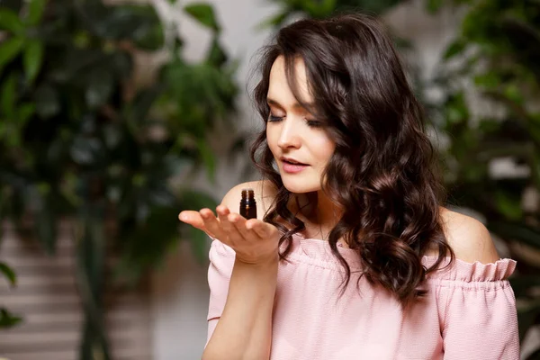 Genç kadın doğal yağ kokularını kokluyor. Yeşil bitkiler içinde pembe bir bluz içinde güzel bir esmer.