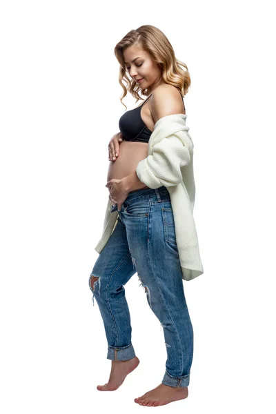 穿着牛仔裤的年轻孕妇面带微笑 表情亲切地抚摸着她的腹部 幸福就是等着孩子 被白色背景隔离 垂直方向 — 图库照片