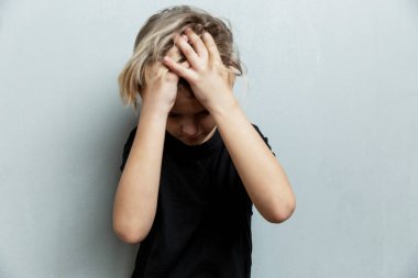 Dehşet içindeki çocuk elleriyle başını tutuyor. Gri arka plan. Stres ve baskı.