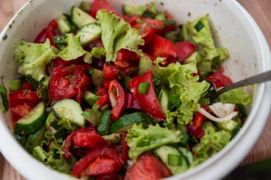 Büyük bir plastik kasede taze sebze salatası. Domates, salatalık, soğan ve otlar. Yakın plan. Vitaminler ve sağlıklı yiyecekler.