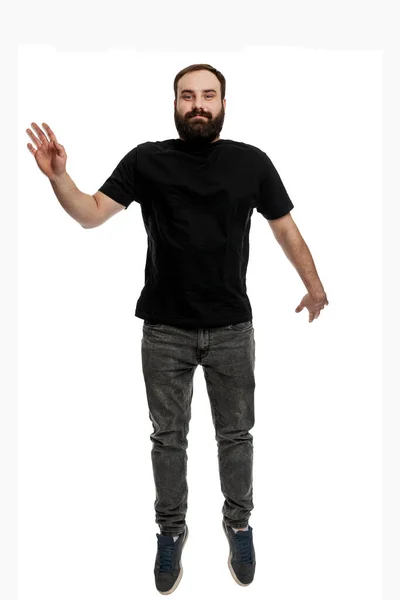 一个留着胡子的年轻人在跳 漂亮的黑发 穿着黑色T恤和灰色牛仔裤 被白色背景隔离 垂直方向 — 图库照片