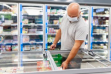 Maskeli bir adam dondurucu bölümünden yiyecek seçer. Bulanık. Koronavirüs salgını.