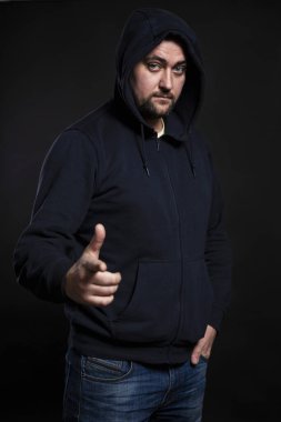 Kapüşonlu koyu renk elbiseli genç adam. Tehlike ve endişe. Siyah arka plan. Dikey.