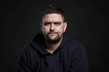 Koyu renk elbiseli, çatık kaşlı bir genç. Endişeler, sorunlar ve stres. Siyah arkaplan.