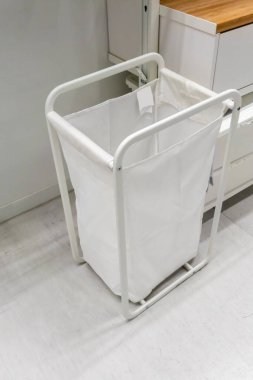 Çamaşır odasında beyaz metal çerçeveli beyaz kumaş sepeti..