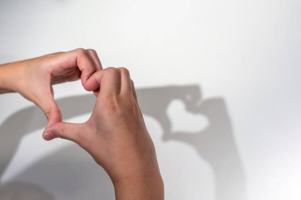 Руки ребенка создают силуэт тени сердца на белом фоне стены. Тень сердца. Понятие любви или Валентины.