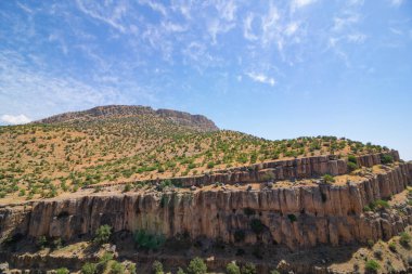 Arka planda tepeler ve uçurumlar olan kanyonun manzarası. Tepelerin üzerinde seyrek ağaçlar. Kanyon arkaplan fotoğrafı.