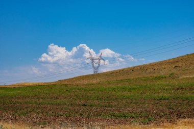 Tarım alanındaki tepede yüksek voltajlı elektrik hatları var..