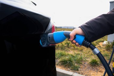 Elektrikli araca bağlandığı için şarj aleti tutan adam. Yüksek kalite fotoğraf. EV vagonu yükleniyor. Karbonsuz. Geleceğin teknolojisi. Sıfır Emmision elektrikli araba. Hızlı AC 42w EV şarj edici.