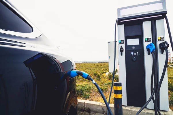 EV car plugged in charger and EV Charger station. Electric car charger station near the highway. Electric car. Zero emission car charging. Carbon free