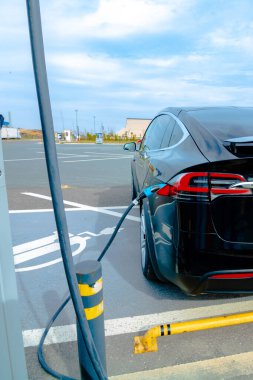 Elektrikli araç EV şarj istasyonunun yakınında şarj oluyor. Sıfır emisyon arabaları. EV şarj aletleri. Alternatif enerji. Hızlı AC EV şarj cihazı. İstasyondaki elektrikli arabanın fişi takılı..