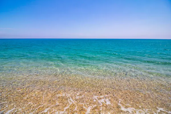 Βότσαλα στην ακρογιαλιά και τυρκουάζ θάλασσα με γαλάζιο ουρανό — Φωτογραφία Αρχείου