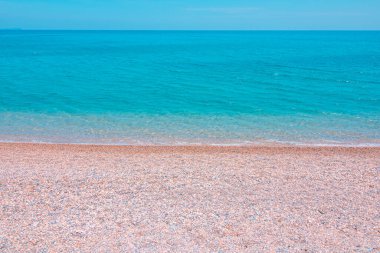 Kumsalda çakıl taşları ve açık mavi gökyüzüne karşı turkuaz deniz. Yaz arkaplanı