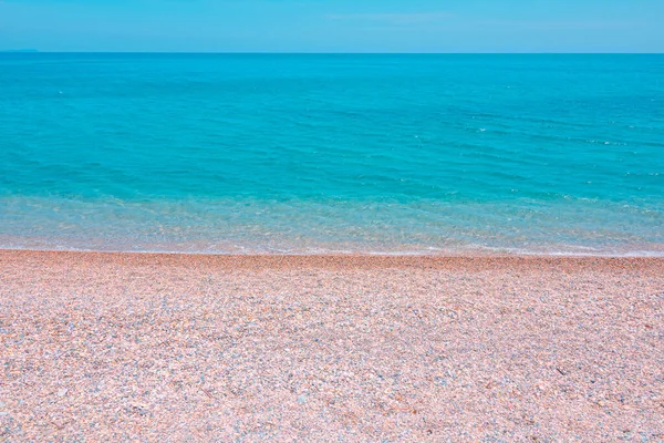 Kumsalda çakıl taşları ve açık mavi gökyüzüne karşı turkuaz deniz. Yaz arkaplanı — Stok fotoğraf