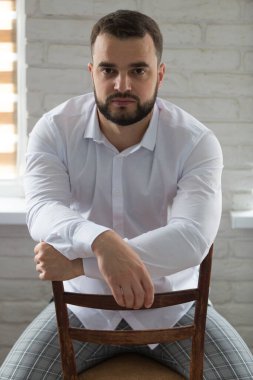 Sandalyede oturan zeki ve ciddi bir gencin portresi. Dikey çerçevelenmiş çekim.