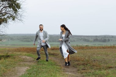 Yaramaz bir çift yeni evli etrafta koşuşturuyor ve kırsalda eğleniyorlar. Düğün gününün mutlu anları. Yatay çerçeveli çekim.