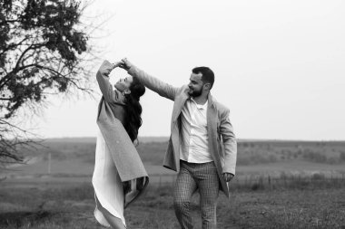 Neşeli yeni evli çiftler kırsalda yürüyorlar. Damat gelinin etrafında dönüyor. Düğün gününün mutlu anları. Yatay çerçeveli çekim