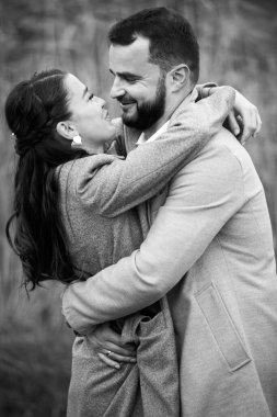 Gri ceketli şık bir çift arka planda nazikçe sarılıyor. Mutlu şehvetli düğün çifti kucaklaşması. Yeni evlilerin romantik anları. Dikey çerçevelenmiş çekim.