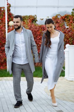 Gri ceketli şık bir çift sonbahar parkında yürüyor. Mutlu şehvetli düğün çifti. Yeni evlilerin romantik anları. Dikey çerçevelenmiş çekim.