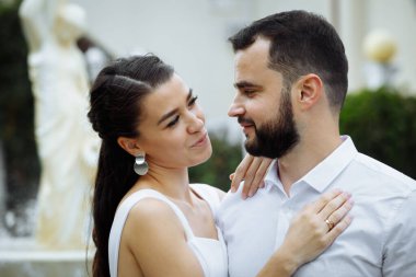 Tarz sahibi çift çeşmenin arka planında nazikçe sarılıyor. Mutlu şehvetli düğün çifti kucaklaşması. Yeni evlilerin romantik anları. Yatay çerçeveli çekim.