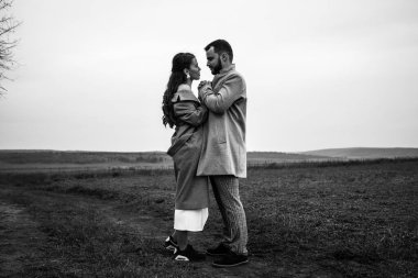 Gri ceketli şık bir çift doğanın arka planında nazikçe sarılıyor. Mutlu şehvetli düğün çifti kucaklaşması. Yeni evlilerin romantik anları. Yatay çerçeveli çekim.