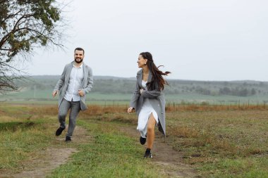 Yaramaz bir çift yeni evli etrafta koşuşturuyor ve kırsalda eğleniyorlar. Düğün gününün mutlu anları. Yatay çerçeveli çekim.