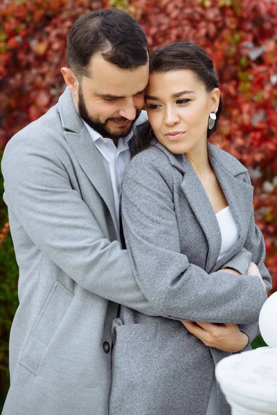 秋の紅葉を背景に 灰色のコートに身を包んだスタイリッシュなカップル 幸せな官能的な結婚式のカップルを受け入れる 新婚旅行のロマンチックな瞬間 縦枠のショット — ストック写真
