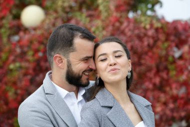 Gri ceketli şık çift sonbahar yapraklarının arka planında nazikçe sarılıyorlar. Mutlu şehvetli düğün çifti kucaklaşması. Yeni evlilerin romantik anları. Yatay çerçeveli çekim.