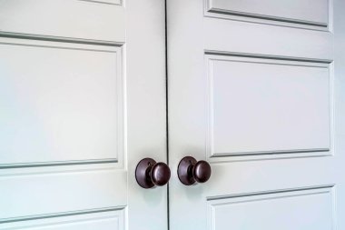 Hinged wooden interior double doors with panelled design and round doorknobs clipart