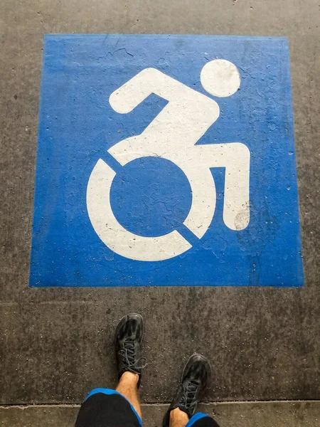 Sinal de deficiente em um espaço de estacionamento com os pés de um homem usando sapatos pretos — Fotografia de Stock