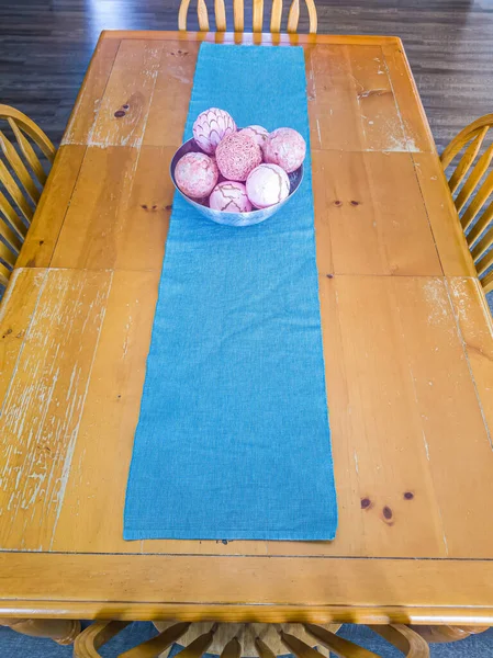 Brown rectangular dining table with blue table runner and bowl with pink balls