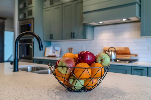 Свежие фрукты внутри корзины из проволоки на острове кухни с раковиной и изогнутым краном — стоковое фото