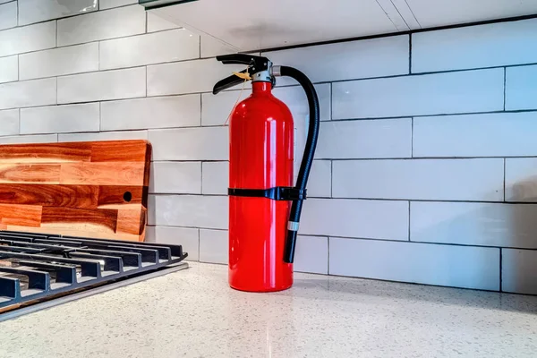 Estintore rosso acceso contro backsplash piastrelle bianche all'interno della cucina domestica — Foto Stock