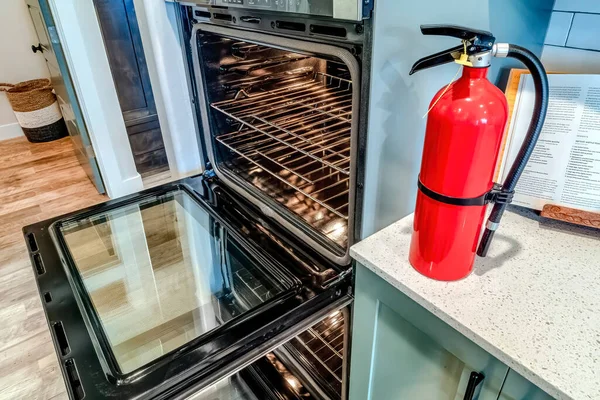 Extintor rojo brillante y horno eléctrico con puertas abiertas dentro de la cocina —  Fotos de Stock