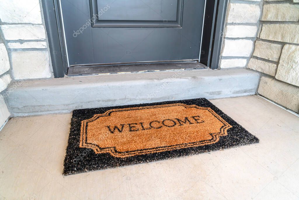 Welcome doormat placed in front of the gray front door of a home entrance
