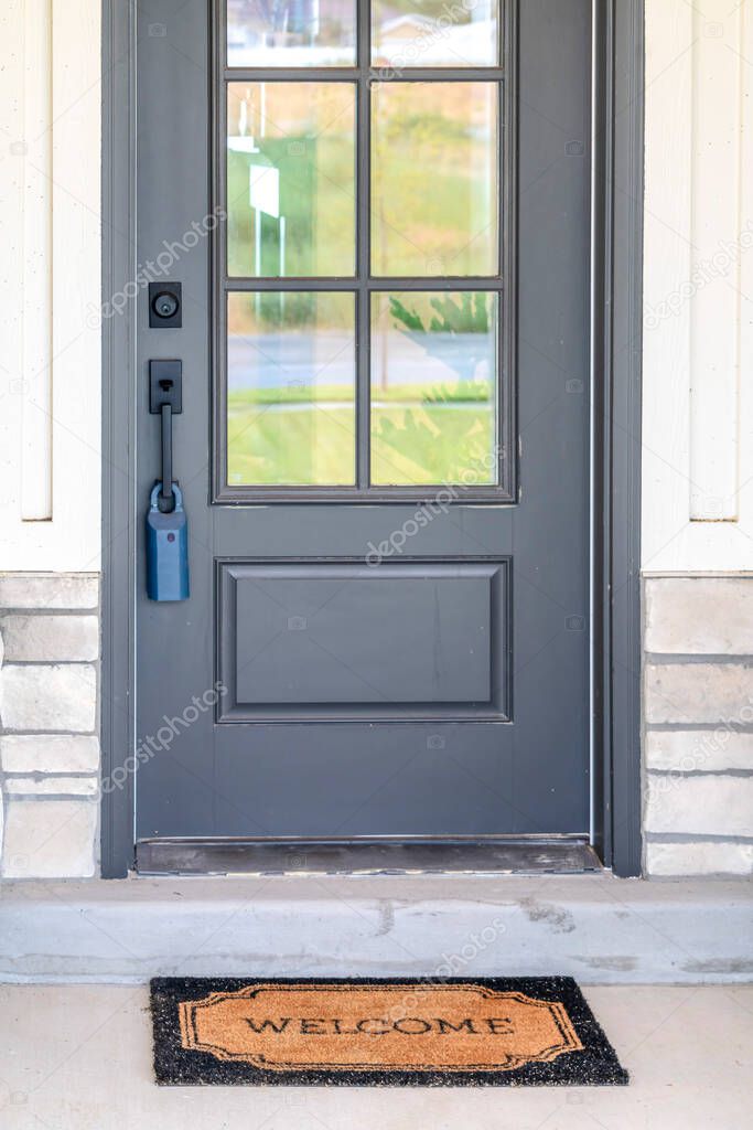 Facade of home with doormat in front of the gray wooden hinged front door