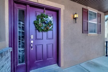 Vivid purple front door with wreath and sidelight at the entance facade of home clipart