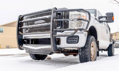 Karlı yolda park etmiş beyaz aracın tamponunda paslı siyah ızgara var.