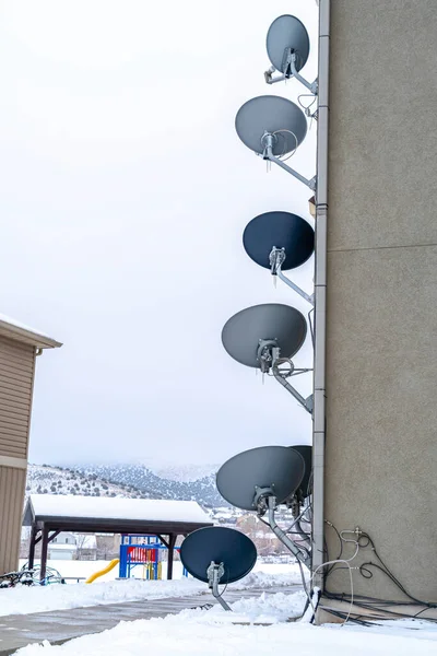 TV antenas parabólicas na parede exterior de um edifício contra a paisagem nevada — Fotografia de Stock