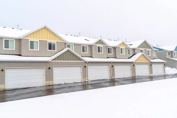Estrada molhada ao longo de portas de garagem brancas de apartamentos contra céu nublado no inverno — Fotografia de Stock