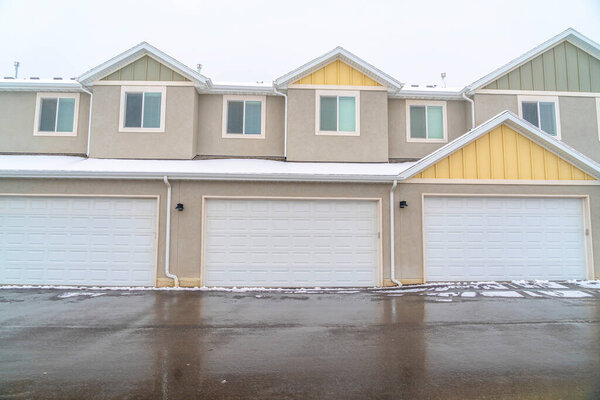 Exterior of apartments with white garage doors along wet snowy road in winter