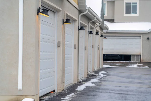 Porte garage e lampade da parete di appartamenti lungo la strada bagnata e innevata in inverno — Foto Stock