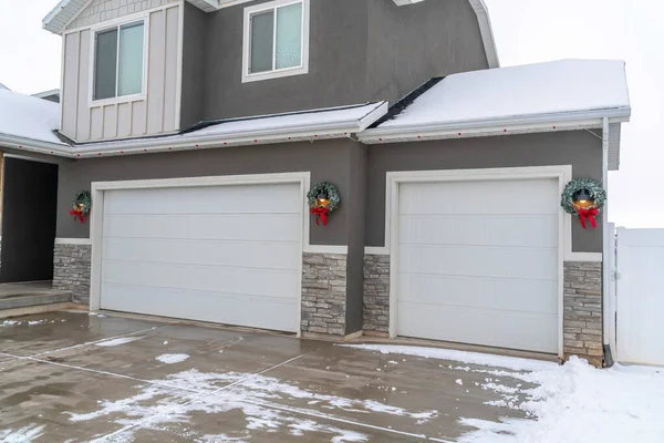Porte da garage bianche e ghirlande natalizie agaist muro grigio di casa con tetto innevato — Foto Stock