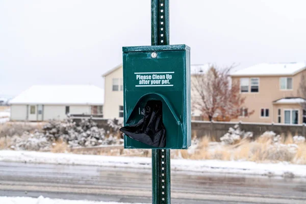 Dog waste station with black pet poop bags against snowy neighborhood landscape