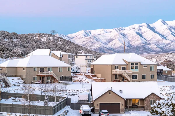 Family homes with snowy roofs and yards against views of mountain and sky